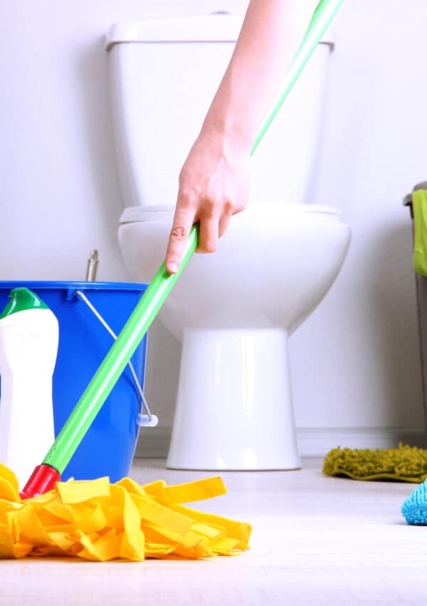 woman with orange mop cleaning bathroom floors