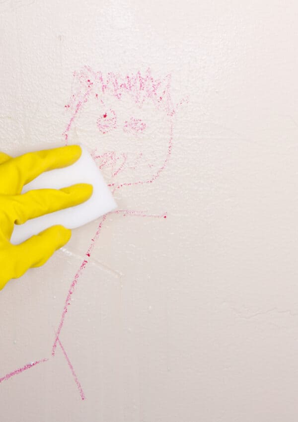 Yellow glove wiping crayon on wall with magic eraser