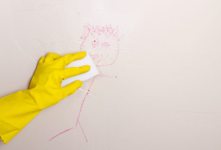 Yellow glove wiping crayon on wall with magic eraser