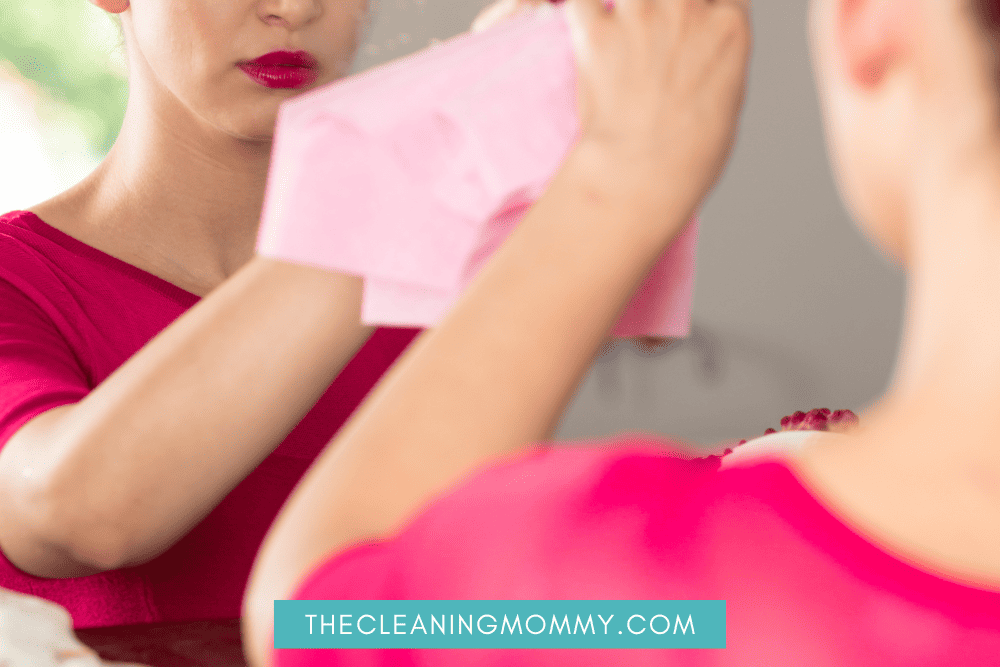 Woman cleaning hazy mirror with pink cloth